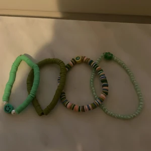 Färgglada armband med smiley-pärlor - Fyra elastiska armband i olika gröna och pastelliga nyanser, dekorerade med små runda pärlor och två smiley-pärlor. Perfekta för att addera färg till din stil.