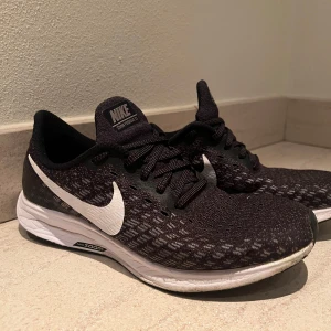 Svarta Nike löparskor med vit sula - Säljer ett par svarta Nike löparskor med vit sula och vit swoosh-logga på sidorna. Skorna har snörning och är tillverkade i syntetmaterial med mesh för bra ventilation. Perfekta för träning eller vardagsbruk.