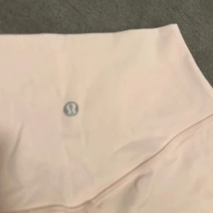 Ljusrosa träningstights shorts från Lululemon farve Strawberry milkshake  - Säljer ett par ljusrosa, högmidjade träningstights shorts från Lululemon. De är stretchiga och har en tight passform, perfekta för gymmet eller yoga. Klassisk Lululemon-logga framtill på linningen.