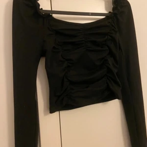 Svart långärmad croppad topp  - Trendig svart långärmad topp med croppad passform och rynkade detaljer framtill. Fyrkantig ringning och lätt puff vid axlarna ger en snygg siluett. Super enkel att styla💗.