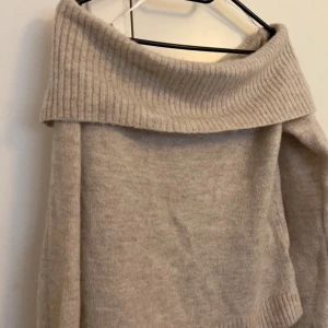 Beige offshoulder stickad tröja  - Mysig beige stickad tröja från Gina Tricot med bred ribbad offshoulder-krage. Perfekt för lager-på-lager och har långa ärmar samt ribbade muddar vid ärmslut och nederkant.