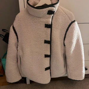 Vit teddyjacka med svarta detaljer - Säljer en fluffig vit teddyjacka från hm.