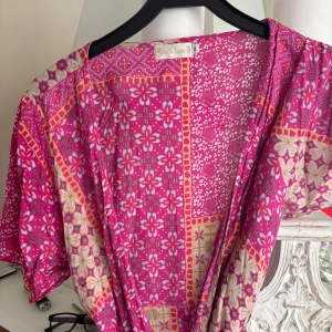 Rosa blommig omlottklänning från Hot lava  - Säljer en superfin rosa omlottklänning från Hot lava med blommigt mönster och knyt i midjan. Klänningen har korta ärmar och är perfekt för sommardagar. Färgglad och lätt att styla!