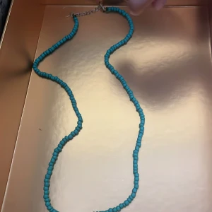 Turkost pärlhalsband - Säljer ett halsband med små turkosa pärlor. Halsbandet har en enkel och stilren design med justerbart spänne i silverfärg. Perfekt för att addera lite färg till din outfit.