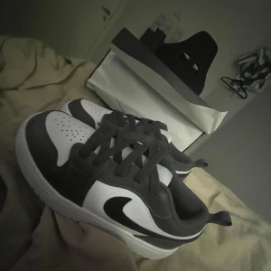 Nike Air Jordans i svart och vitt - Säljer ett par Nike Air Jordans i svart och vitt med klassisk swoosh på sidan. Skorna har snörning och rund tå, och kommer med originalkartong. Perfekta för dig som gillar streetwear och vill ha en ikonisk sneaker i garderoben.