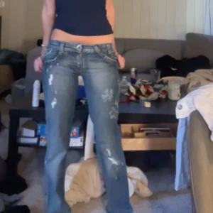 Levis jeans med broderade detaljer - Säljer ett par blå Levis jeans med broderade mönster och slitningar. Byxorna har låg midja och raka ben, samt unika broderier i olika färger på ena benet. De är straight men sitter mer som bootcut🥰