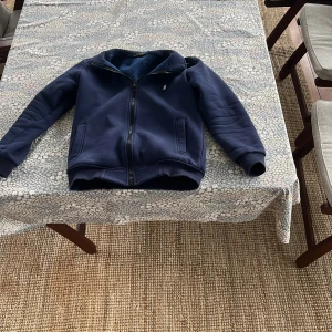 Mörkblå fleecefodrad jacka från Polo Ralph Lauren - Mörkblå jacka med dragkedja från Polo Ralph Lauren. Man kan ha kragen uppe eller nere mycket bra fickor och den är fortfarande mjuk på in sidan vilket menas att den inte har blivit tvättad många gånger,passar till allt och är en allmänt grisch/snygg hoodie, passar folk mellan 152-161 cm/ priset är ej huget i sten så kom med funderingar och prisförslag.men som ni såg har den lite fläckar på armän som ej går att få bort tror jag 