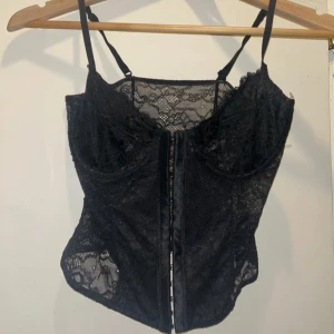 Svart spetskorsett med smala axelband - Säljer en svart korsettopp i spets med smala justerbara axelband och bygel vid bysten. Toppen har vacker spets både fram och bak. Toppen passar S/XS☺️