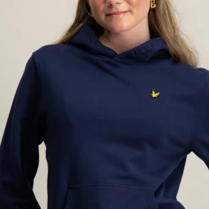 Mörkblå hoodie från Lyle & Scott - Säljer en mörkblå hoodie från Lyle & Scott med klassisk gul logga på bröstet. Tröjan har huva, magficka och långa ärmar. Perfekt för en avslappnad stil och enkel att matcha med jeans eller leggings.