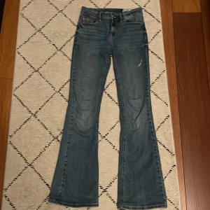 Blå bootcut jeans från Vero Moda - Säljer ett par klassiska blå bootcut jeans från Vero Moda. Jeansen har en lätt slitning på låret som va där när jeansen köptes och normal passform med utsvängda ben. Perfekta till vardags för en avslappnad men snygg look.