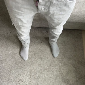 Ljusgrå jeans från Dsquared2 - Säljer ett par ljusgrå jeans från Dsquared2 med klassisk femficksdesign och diskreta slitningar på benen. Jeansen har knappgylf och Dsquared2-logga vid gylfen. Perfekta för dig som gillar stilrena och trendiga jeans. De har målarfärg och utsuddad målarfärg som är en del av designen. Jag är 160 cm lång och som ni ser på bilderna passar de perfekt. Skriv om ni har några frågor