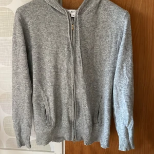 Grå hoodie med dragkedja från Barlucio - Mjuk och stilren grå kashmir hoodie från Barlucio i storlek S. Tröjan har dragkedja framtill, huva och två fickor. Perfekt för lager-på-lager och passar till många olika outfits. Varan är typ som ny! 