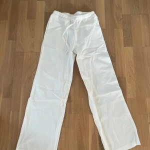 Vita linnebyxor med dragsko - Säljer ett par vita linnebyxor med avslappnad passform och dragsko i midjan. Perfekta för varma dagar och ger en luftig känsla. Byxorna har raka ben och enkel design som passar till mycket. 