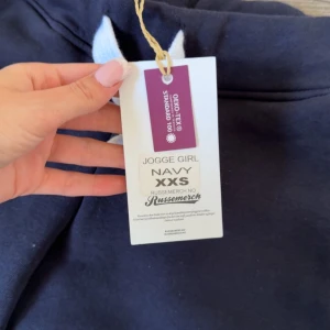 Mörkblå mjukisbyxor Jogge Girl - Mörkblå mjukisbyxor från Russmerch med vit dragsko i midjan och fickor på sidorna. Perfekta för en avslappnad stil och bekväma dagar. Byxorna har en klassisk passform och är tillverkade i mjukt material.