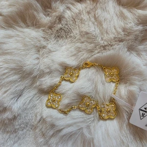 Guldpläterad Fyrklöver-armband - Armband i guld med flera fyrklöverformade länkar, dekorerade med gnistrande stenar. 