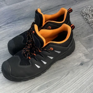 Svarta sneakers med orange detaljer - Säljer ett par svarta sneakers med orange insida och detaljer. Skorna har snörning och reflekterande trianglar på sidorna. Perfekta för dig som vill ha en sportig och bekväm stil.  helt nya 