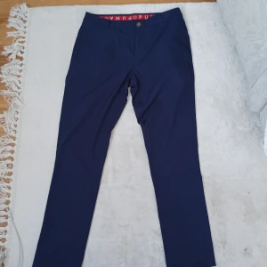 Mörkblå byxor från Puma - Snygga mörkblå byxor från Puma med diskret logga på bakfickan och röd detalj på insidan av midjan. Byxorna har normal passform och raka ben, perfekta för en sportig och stilren look. Jätte sköna finbyxor.