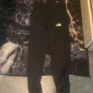 Svarta mjukisbyxor från The North Face - Svarta mjukisbyxor från The North Face med logga på vänster lår. Byxorna har en enkel och stilren design med resår i midjan och raka ben. Perfekta för en avslappnad stil eller till träning. Ny pris 1000kr