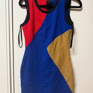 Färgglad ärmlös klänning med geometriskt mönster - Säljer en cool ärmlös klänning med geometriska fält i blått, rött och beige. Klänningen har en tight passform och rund halsringning. Perfekt för dig som gillar färg och vill sticka ut.