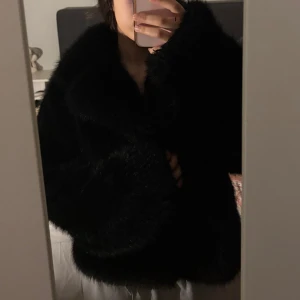 Svart pälsjacka med oversized passform - Säljer en svart, fluffig pälsjacka med oversized passform. Jackan har lång ärm och bred krage, perfekt för att hålla värmen och ge en cool look. Passar dig som vill sticka ut och hålla stilen under kallare dagar.