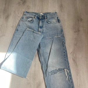 Ljusblå jeans med slitningar - Säljer ett par ljusblå jeans med hög midja och raka ben från Gina Tricot. Jeansen har slitna detaljer på framsidan och är lite längre så dom faller snyggt nere vid fötterna.