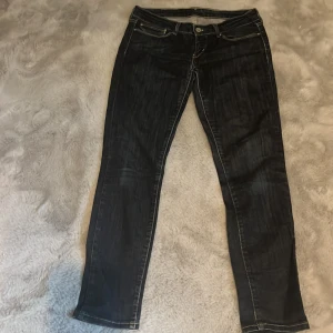 Mörkblå jeansbyxor Levis 501 - Säljer ett par klassiska mörkblå Levis 501 jeans med raka ben och normal passform. Byxorna har fem fickor, knappgylf och tydliga kontrastsömmar. Perfekta för en tidlös stil och passar till det mesta.