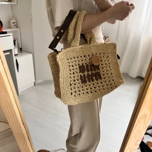 Beige virkad handväska med text - Superfin beige virkad handväska med bruna detaljer och texten 'beach witch' framtill. Väskan har två handtag och en avtagbar axelrem i mörkbrunt. Perfekt för sommarens alla äventyr!