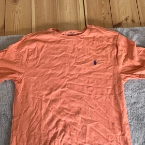 Orange t-shirt från Polo Ralph Lauren - Säljer en orange t-shirt från Polo Ralph Lauren med klassisk passform och liten broderad logga på bröstet. T-shirten är kortärmad och tillverkad i mjuk bomull. Perfekt för en avslappnad stil.