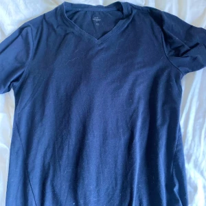 Mörkblå v-ringad t-shirt från A-Z - Säljer en mörkblå t-shirt från A-Z med v-ringning. T-shirten har korta ärmar och är tillverkad i mjuk bomull, perfekt för en avslappnad stil.