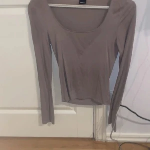 Beige långärmad topp med rund hals - Säljer en beige långärmad topp med rundad, djup ringning. Tunn och mjuk i materialet, perfekt för lager-på-lager eller som den är. Enkel och stilren design som passar till mycket.