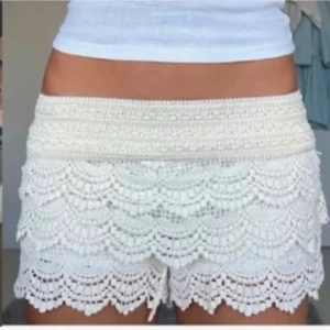 Spets shorts  - Säljer ett par vita virkade shorts med vacker spets och volangkant. De har elastisk midja och ett feminint, bohemiskt utseende. Perfekta för varma dagar och ger en romantisk touch till outfiten.