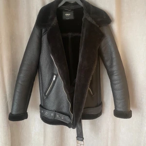 Svart pälsfodrad jacka från ONLY - Säljer en svart jacka från ONLY med mjukt pälsfoder och bred krage. Jackan har dragkedja, två snedställda fickor med dragkedja och bälte i midjan. Perfekt för kyliga dagar och ger en cool look.