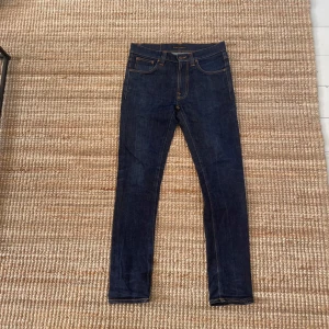 Mörkblå  jeans från Nudie Jeans - Säljer ett par mörkblå lean dean jeans från Nudie Jeans med klassiska orange sömmar och femficksdesign. Perfekta för dig som gillar en slim passform👍
