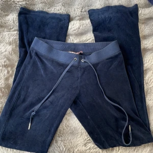 Mörkblå velourbyxor från Juicy Couture - Mörkblå mjukisbyxor från Juicy Couture i mjuk velour med bred resår och dragsko i midjan. Klassisk modell med raka ben och diskret logga på insidan. Perfekta för en avslappnad och trendig look. Det är ett par vintage juicy vilket är väldigt ovanligt nu för tiden, har använt fåtal gånger. Jätte low tycker jag att de är!🥰💓