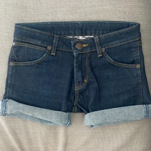 Lågmidjade jeansshorts  - Säljer ett par mörkblå jeansshorts från Wrangler. Dessa jeansshorts är aldrig använda, de har vikts upp så ifall man vill ha längre jeansshorts är det endast att vika ned dom! Så enkelt😊! Storleken är W26 men skulle säga sitter som Xs! Kontakta vid frågor eller funderingar😇