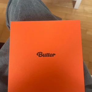 Butter (Peaches version) av BTS - Säljer BTS album 'Butter' i Peaches-versionen. Boxen är orange och innehåller CD, photocard, och inlagor med texten 'Permission to Dance'. Perfekt för samlare och fans av K-pop och BTS.