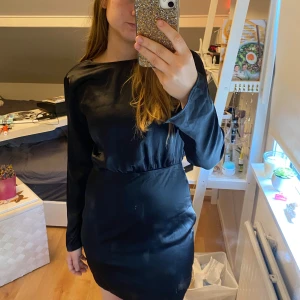 Klänning med öppen rygg - Säljer en svart satinklänning från Gina Tricot med lång ärm och snygg öppen rygg. Klänningen har en elegant, enkel design och är tillverkad i ett glansigt satinmaterial. Perfekt för dig som vill ha en stilren look med en twist.