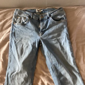 Ljusblå jeansbyxor - Säljer ett par klassiska ljusblå jeans med fem fickor och gylf med dragkedja och knapp. Jeansen har raka ben och normal passform, perfekta till vardags. Snygga detaljer med nitar vid fickorna. ca 80 cm i benen