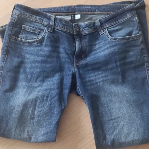Blå bootcut jeans från H&M Divided - Säljer ett par klassiska blå jeans från H&M Divided. Jeansen har fem fickor, knapp och dragkedja framtill samt snygga slitningar för en cool look. Perfekta till sneakers eller boots. Inga slitningar där nere i byxorna (se bild 3). Kom privat för mått eller fler bilder. 