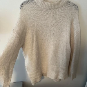 Beige stickad polotröja - Mysig beige stickad polotröja med bred krage och långa ärmar. Perfekt för kyliga dagar och enkel att matcha med olika outfits. Tröjan har en avslappnad passform och ribbade detaljer vid krage, ärmslut och nederkant. 