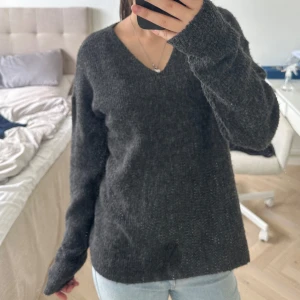 Mörkgrå stickad tröja från ONLY - Mysig mörkgrå stickad tröja från ONLY med v-ringad halsringning. Tröjan har lång ärm och en klassisk, enkel design som passar perfekt till jeans eller kjol. Perfekt för kyligare dagar.