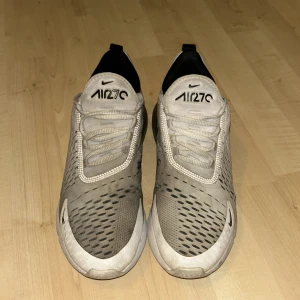 Nike air max 270 - Nike Air Max 270 sneakers i grått och svart med vita detaljer. Skorna är inte sönder eller rivna. på bilden är skorna lite blöta derför så ser det lite grå färgad ut, men det är ingen fara för det betyder att du kommer få skorna fräscha när du köper de. Har använt skorna i ungefär 8 månader nu så det är inte så slitna.
