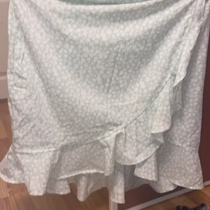 Ljusgrön omlottkjol med volang - Säljer en ljusgrön omlottkjol med diskret mönster och volang längs nederkanten. Kjolen har en feminin och flowy känsla, perfekt för varmare dagar. Omlottmodellen ger en snygg detalj och kjolen är lätt att matcha med olika toppar.