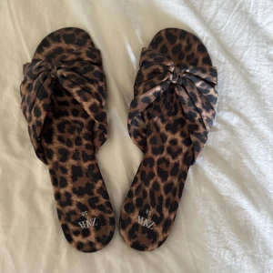 Leopardmönstrade sandaler från Zara - Säljer ett par sandaler från Zara med leopardmönster och knutdetalj framtill. Skorna har platt sula och öppen tå.