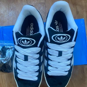 Adidas Campus sneakers svart/vit - Säljer ett par Adidas Campus storlek 39 i svart  med vita ränder. Extra svarta snören och orginalkartong tillkommer. Aldrig använda och helt nya! Säljer de eftersom de är för småa för mig.  Rekommenderas verkligen!  Storlek 39 (hör av er om ni har frågor)