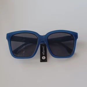 Blåa solglasögon med fyrkantig form - Snygga solglasögon från Prestige 5 i en matt blå färg med breda skalmar och fyrkantiga svarta glas. Skandinavisk design och modern look, perfekta för att sticka ut i solen.