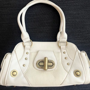 Snygg vit y2k handväska - Snygg  Y2K handväska med många fickor och mycket utrymme. Passar perfekt att ha till skolan. Den är väl använd och har imperfektioner. (Knappt märkbara blåa märken på under sidan, handtaget där framme har jag fixat/sytt, syns knappast) 