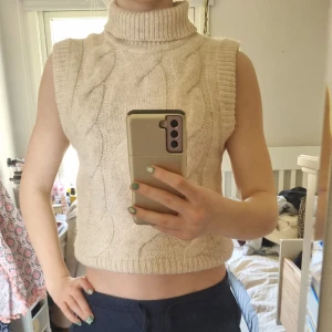 Beige stickad väst med polokrage från Gina Tricot - Säljer en beige stickad väst från Gina Tricot med polokrage och grovt flätmönster. Västen är ärmlös och har ribbade kanter vid ärmhål, hals och nederkant. Perfekt att styla över en skjorta eller långärmad tröja.Har användit några gånger men i nyskick.  Frakt ingår inte. Säljer för att jag har växt ur dem. 