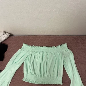 Mintgrön offshoulder blus - Säljer en söt mintgrön blus med offshoulder-modell och långa ärmar. Blusen har smockdetaljer upptill och nedtill som ger en fin passform. Perfekt för vår och sommar! Den är i storlek Men ganska stretchig 