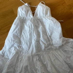 Vit sommarklänning med broderade blommor - Säljer en vit klänning med tunna axelband och v-ringning. Klänningen har broderade blommor och volang nertill💞